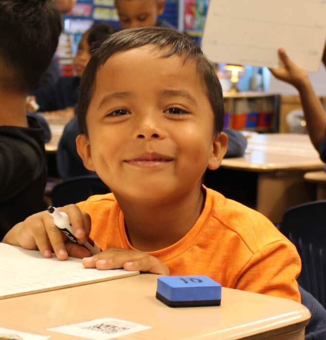 male elementary student in writing on small white board in classroom