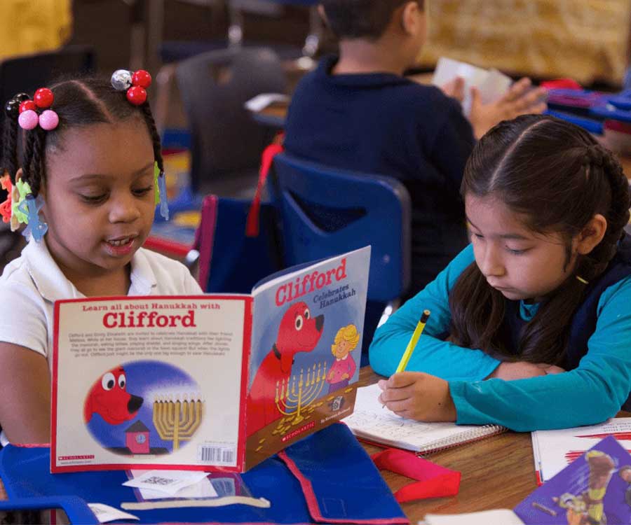 two little girls reading and working on school work at desk