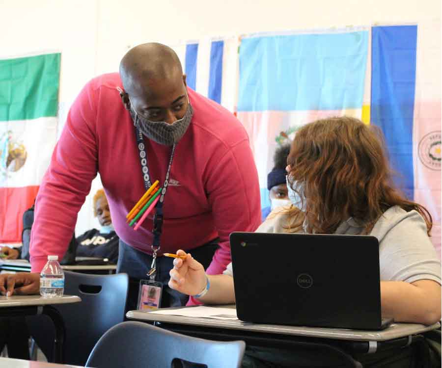 male teacher helping student while doing work on their computer at desk