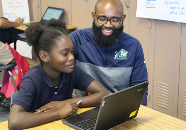 teacher helping student while she works on her computer